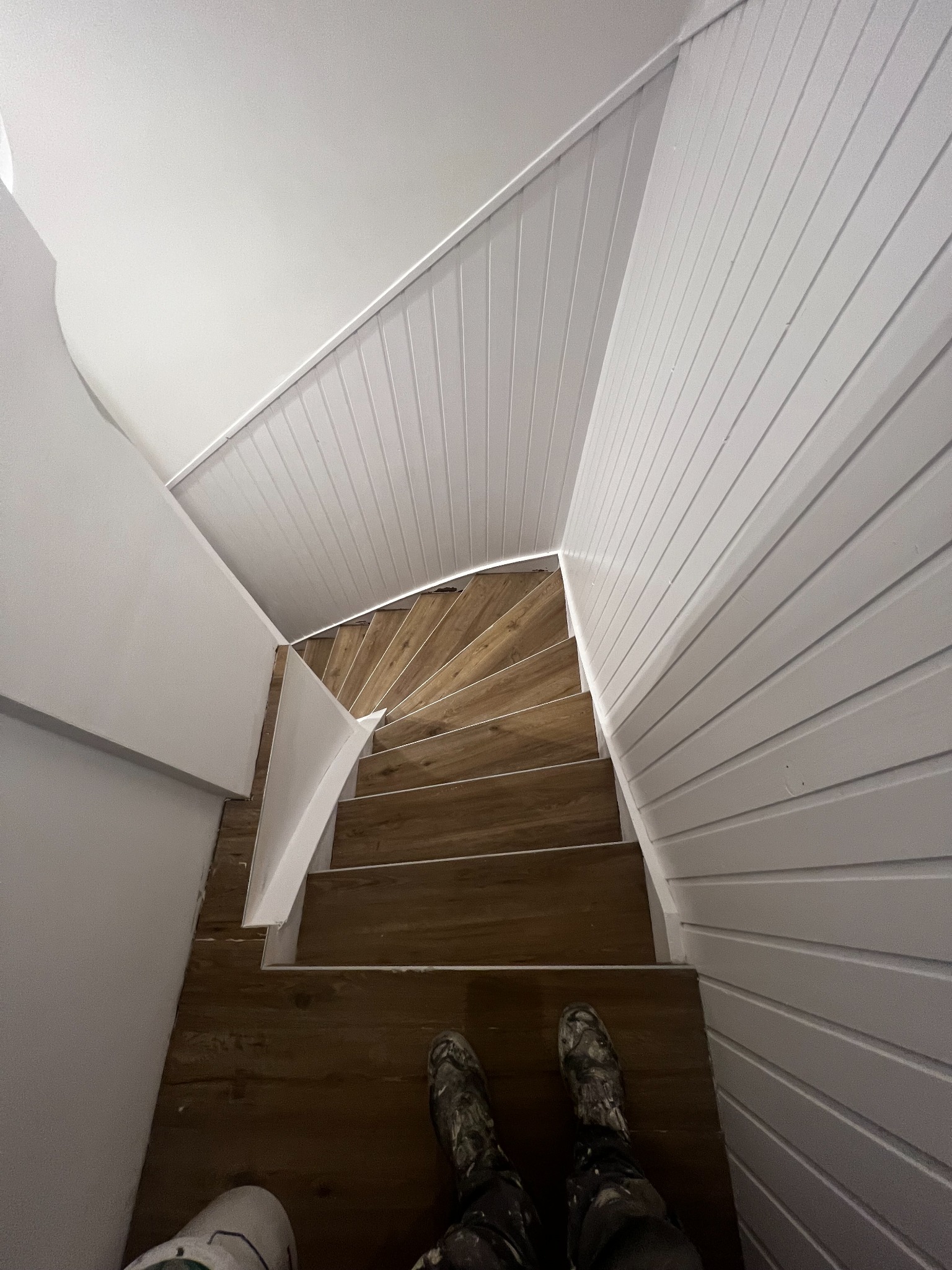 Widok z góry na drewniane schody spiralne po remoncie w domu w Ostrowie Wielkopolskim, z widocznymi pomalowanymi na biało ścianami z boazerii.