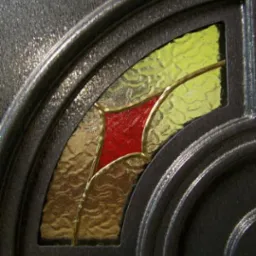 Fragment drzwi z ozdobnym, kolorowym wypełnieniem w kształcie wachlarza, z czerwonym akcentem pośrodku, widziany z bliska w Pleszewie.