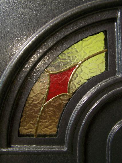 Fragment drzwi z ozdobnym, kolorowym wypełnieniem w kształcie wachlarza, z czerwonym akcentem pośrodku, widziany z bliska w Pleszewie.