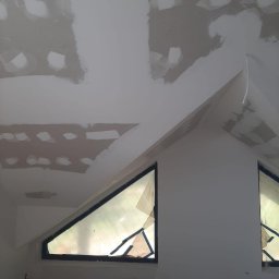 Filip Kowalski - Poddasze w Nowogardzie w trakcie prac wykończeniowych, widoczne fragmenty sufitu i ściany z nałożonymi warstwami wyrównującymi, okna zabezpieczone folią malarską, przygotowanie do dalszych etapów...