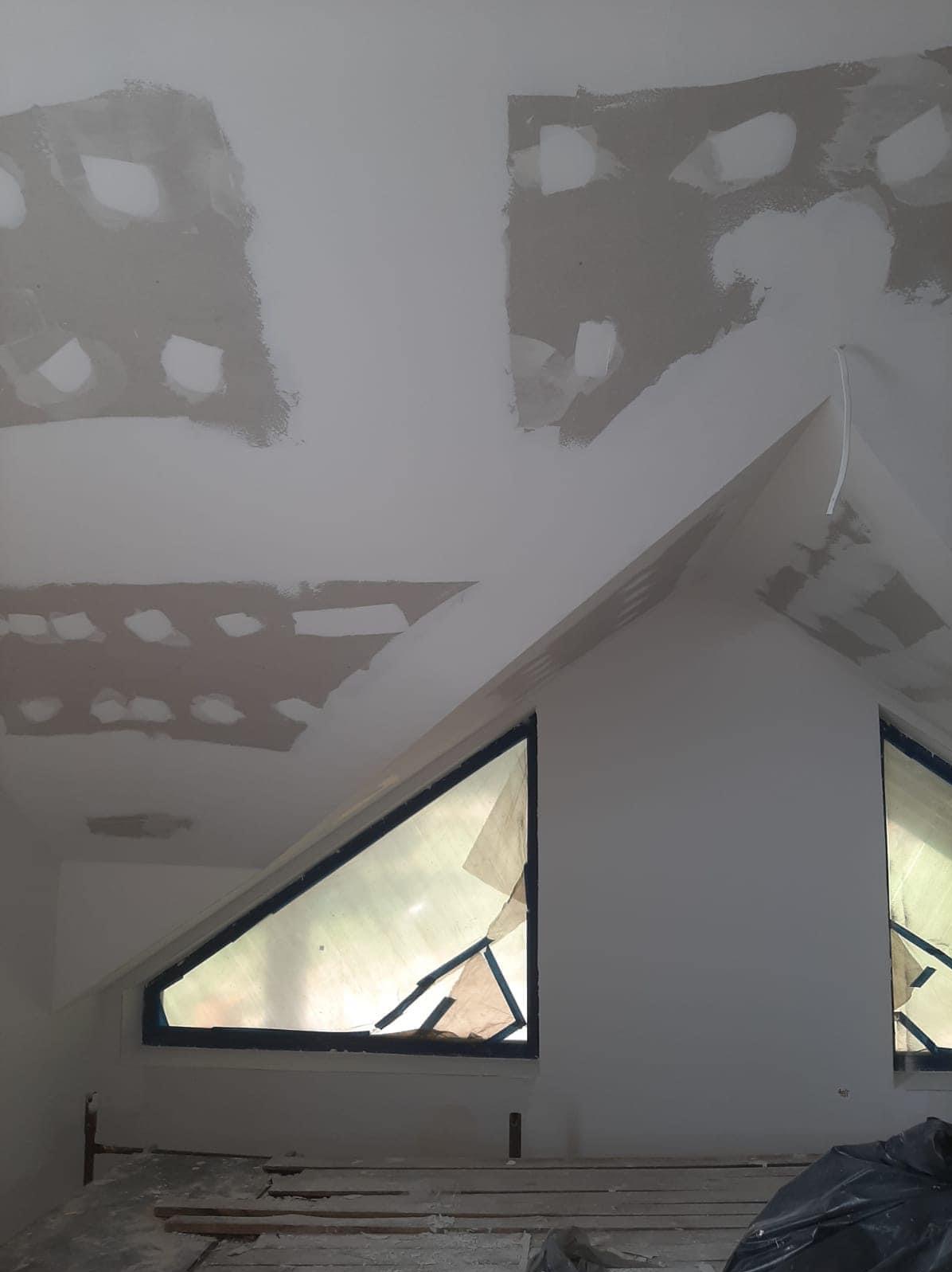 Poddasze w Nowogardzie w trakcie prac wykończeniowych, widoczne fragmenty sufitu i ściany z nałożonymi warstwami wyrównującymi, okna zabezpieczone folią malarską, przygotowanie do dalszych etapów...