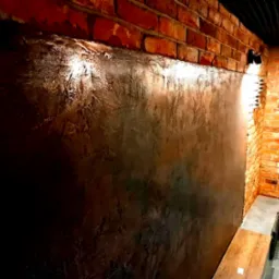 Dekoracyjna ściana z efektem betonu architektonicznego w pomieszczeniu z ceglanymi ścianami i oświetleniem punktowym.