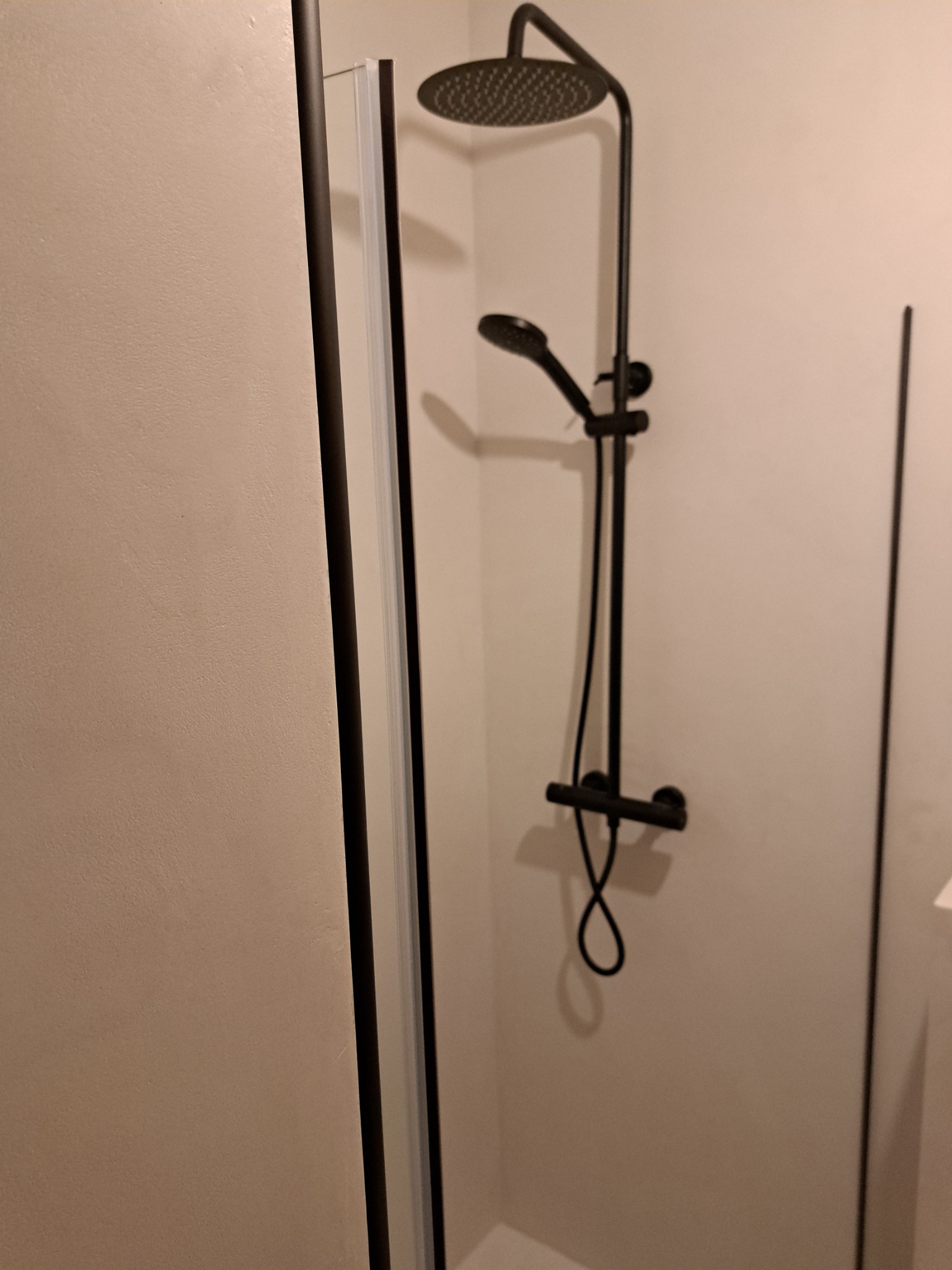 Czarny zestaw natryskowy z deszczownicą i słuchawką, zamontowany w kabinie prysznicowej w Świeciu. Widoczna część ściany wykończona gładzią.