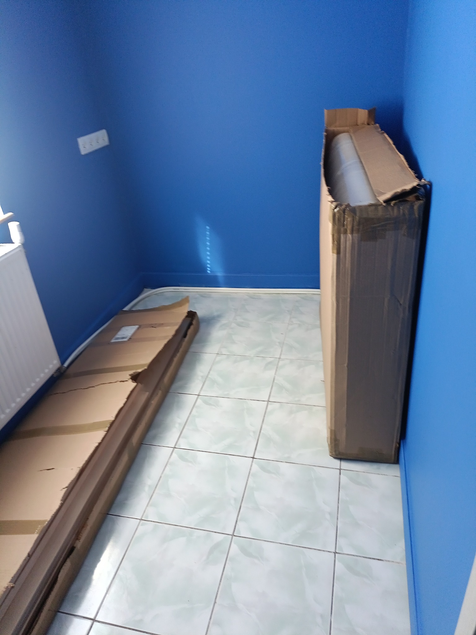 Pudła z sufitem napinanym w rogu pokoju z niebieskimi ścianami i białą podłogą z płytek.