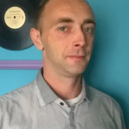 Portret mężczyzny w szarej koszuli na tle turkusowej ściany z fioletową ramką i płytą winylową.