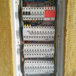 Rozdzielnica elektryczna z zabezpieczeniami nadprądowymi, ogranicznikami przepięć i przewodami w ścianie ocieplonej wełną mineralną.