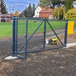 Nowo zamontowana, stalowa brama panelowa z podmurówką w Gryfowie Śląskim. Widoczny agregat prądotwórczy i częściowo biały samochód dostawczy. W tle budynki mieszkalne i zieleń.