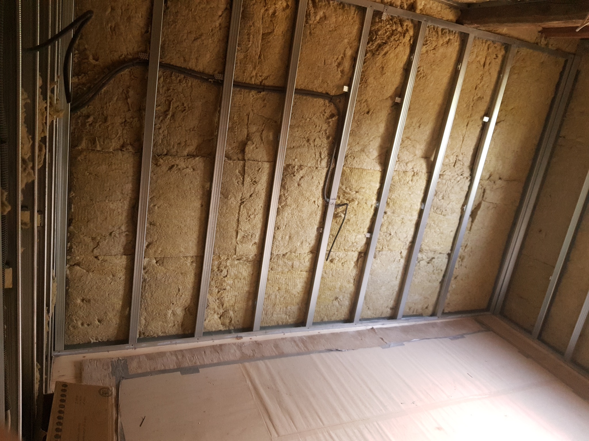 Ściana poddasza w trakcie izolacji wełną mineralną, widoczne metalowe profile konstrukcyjne i instalacja elektryczna w peszlach.