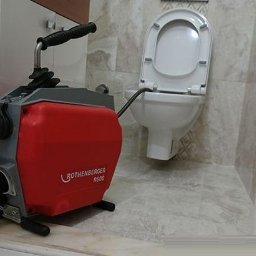Hydraulik - Elektryczna maszyna do udrażniania rur Rothenberger R600 podłączona do toalety w łazience wyłożonej marmurowymi płytkami.
