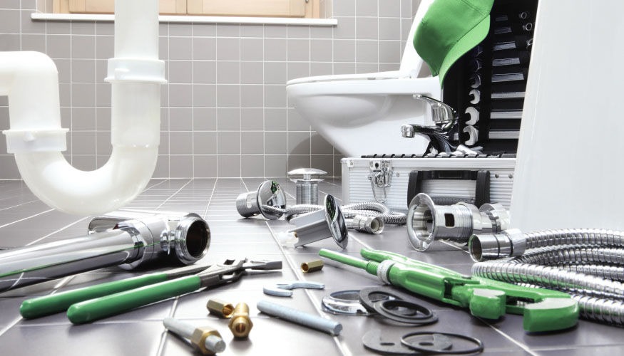 Rozłożone narzędzia hydrauliczne i elementy instalacji wodnej na podłodze łazienki z widoczną toaletą i rurami odpływowymi