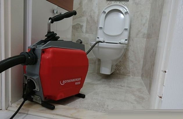 Elektryczna maszyna do udrażniania rur Rothenberger R600 podłączona do toalety w łazience wyłożonej marmurowymi płytkami.