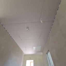 Mariusz Filek - Montaż płyty karton gips na suficie w korytarzu w Ślemieniu, widoczne profile i otwory na wkręty, sufit przygotowany do dalszych prac wykończeniowych.