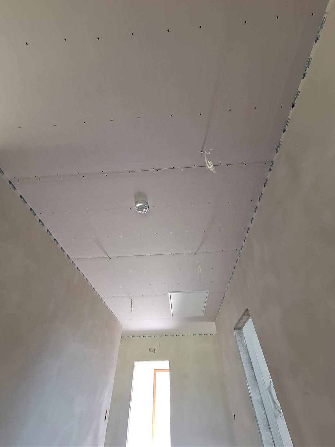 Montaż płyty karton gips na suficie w korytarzu w Ślemieniu, widoczne profile i otwory na wkręty, sufit przygotowany do dalszych prac wykończeniowych.