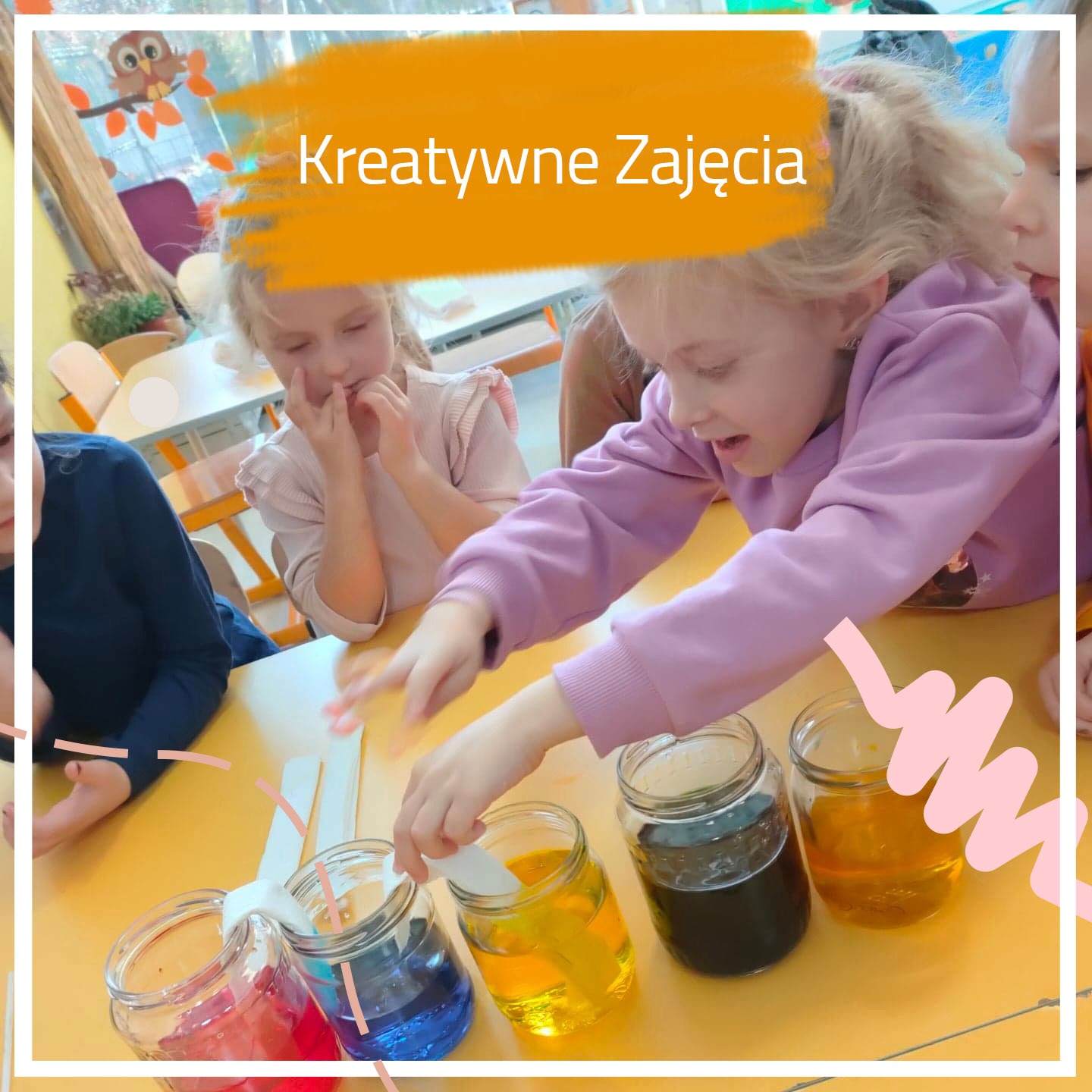 Dziewczynka w fioletowej bluzie miesza farby w słoikach na żółtym stole, obok inne dzieci obserwują eksperyment, w tle dekoracja z sową.