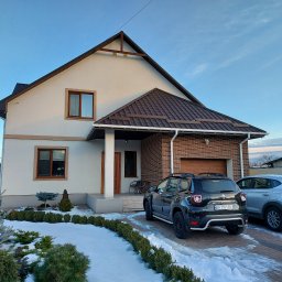 Baronin Development - Ocieplony dom jednorodzinny z elewacją w kolorze kremowym i brązowym dachem, z garażem obłożonym czerwoną cegłą klinkierową, widok z zewnątrz w zimowej scenerii z dwoma zaparkowanymi samochodami.