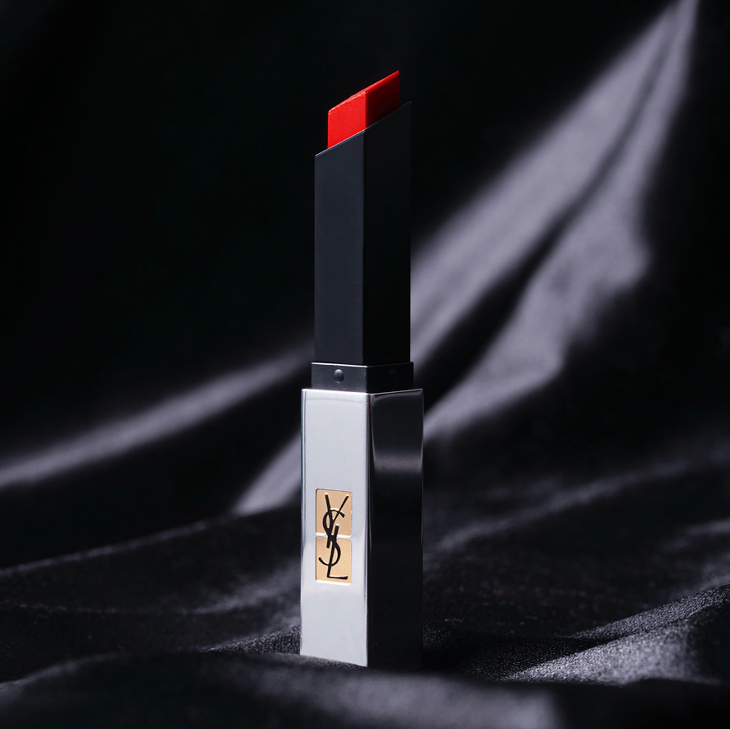 Szminka w srebrno-czarnym opakowaniu z logo na tle czarnej, satynowej tkaniny.