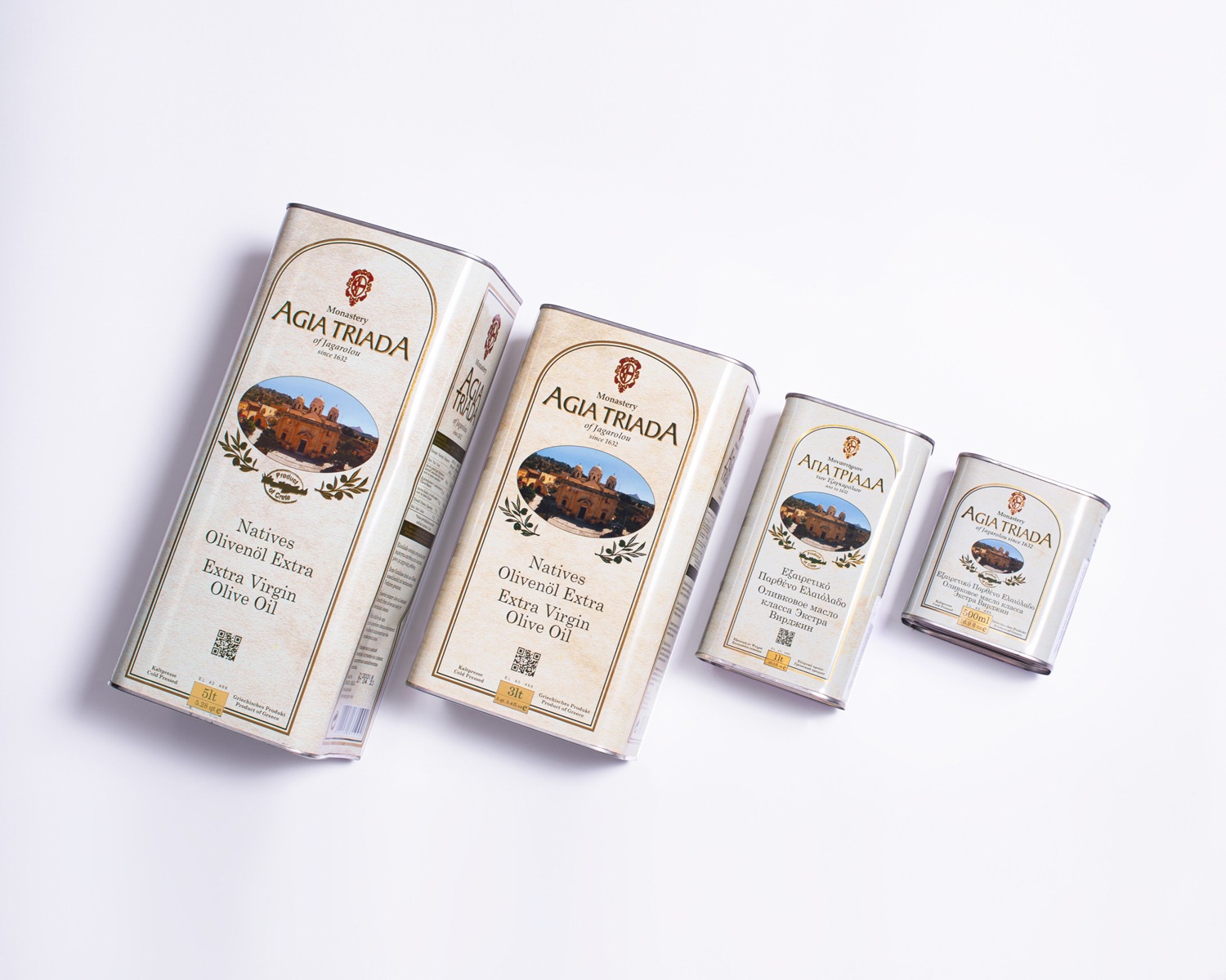Cztery puszki oliwy z oliwek Agia Triada różnej wielkości, ustawione ukośnie na białym tle, prezentujące etykiety z wizerunkiem klasztoru i napisem 'Extra Virgin Olive Oil'.