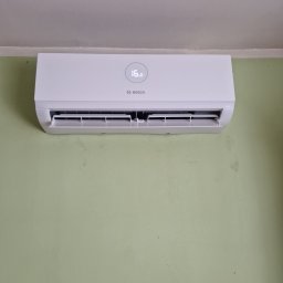 Eco green-Tech - Biała jednostka klimatyzacyjna Bosch zamontowana na zielonej ścianie, wyświetlająca temperaturę 16 stopni Celsjusza.