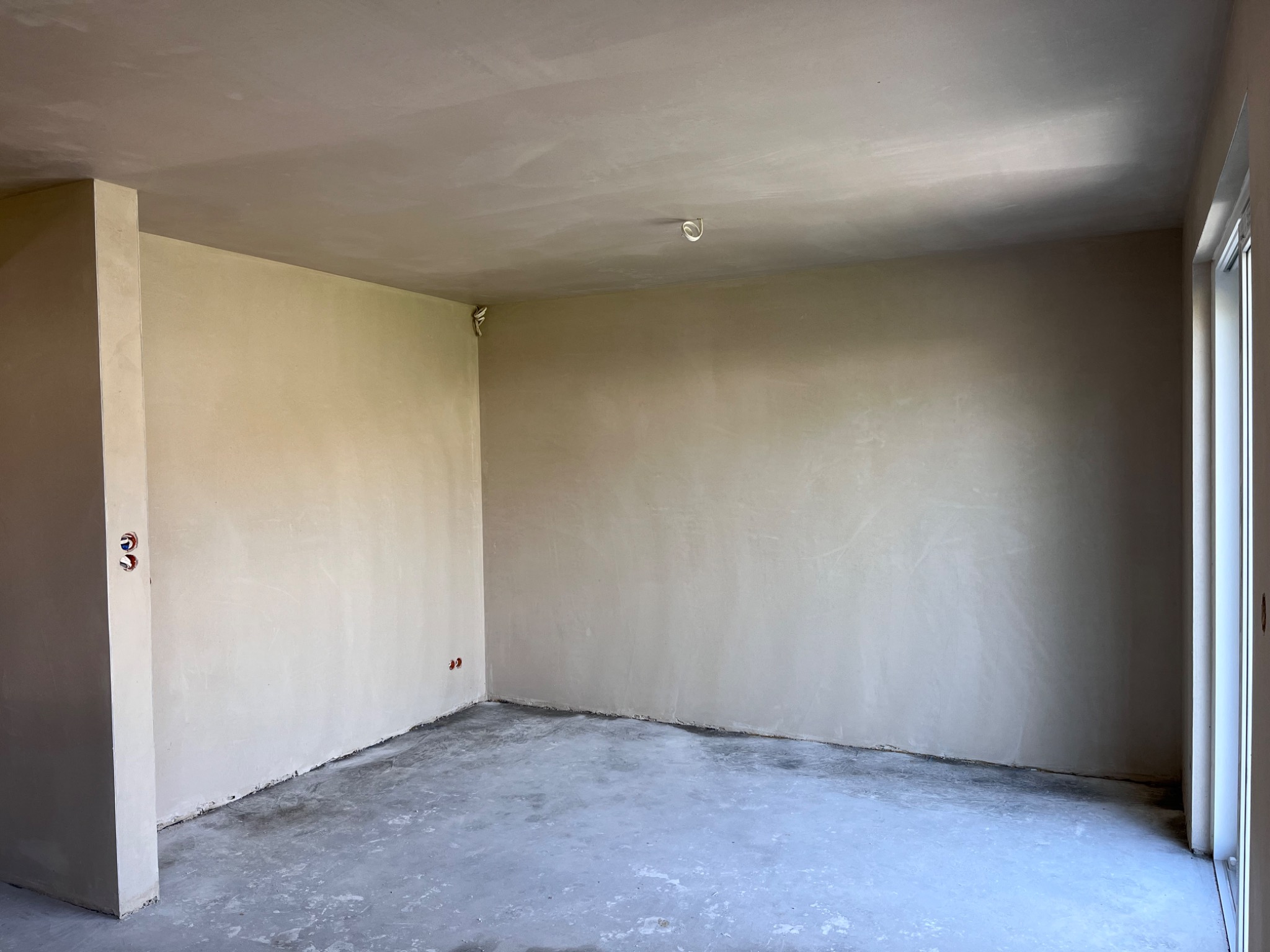 Wnętrze po nałożeniu gładzi gipsowej, widoczne wystające kable elektryczne i fragment okna.