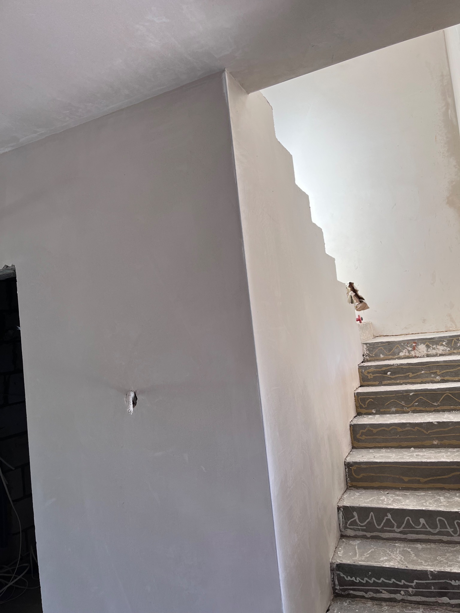 Świeżo otynkowana ściana w klatce schodowej z surowymi schodami, widoczne zabezpieczone kable elektryczne w ścianie.
