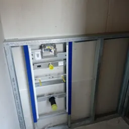 Stelaż podtynkowy Geberit Duofix zamontowany w łazience, widoczne rury kanalizacyjne i elementy mocujące, ściany w trakcie zabudowy płytami gipsowo-kartonowymi.