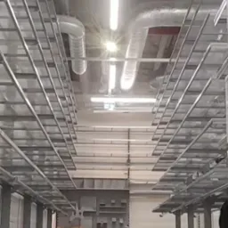 Sufit z instalacjami wentylacyjnymi i oświetleniem w surowym, industrialnym stylu. Widoczna metalowa konstrukcja podwieszana i rury wentylacyjne.