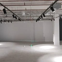 Electro Alpinist Dominik Wójcik - Wnętrze komercyjne z surowym betonem, oświetleniem szynowym i laserowym niwelatorem wskazującym poziom. Widoczne instalacje pod sufitem.