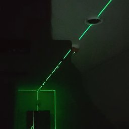 Electro Alpinist Dominik Wójcik - Zielony laser krzyżowy w ciemnym pomieszczeniu, wyznaczający linie na ścianach i suficie, prawdopodobnie podczas prac instalacyjnych lub pomiarowych.