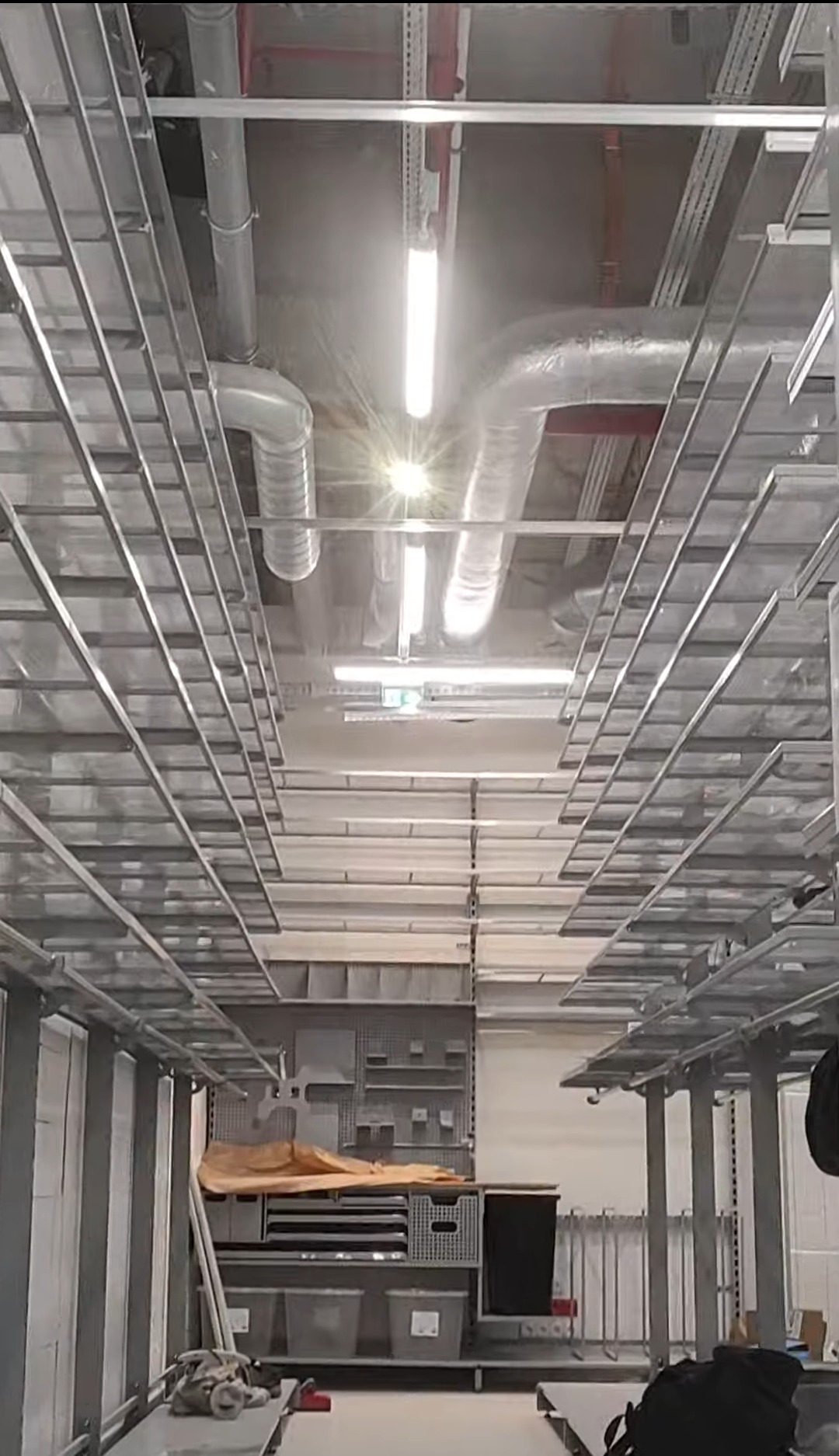 Sufit z instalacjami wentylacyjnymi i oświetleniem w surowym, industrialnym stylu. Widoczna metalowa konstrukcja podwieszana i rury wentylacyjne.