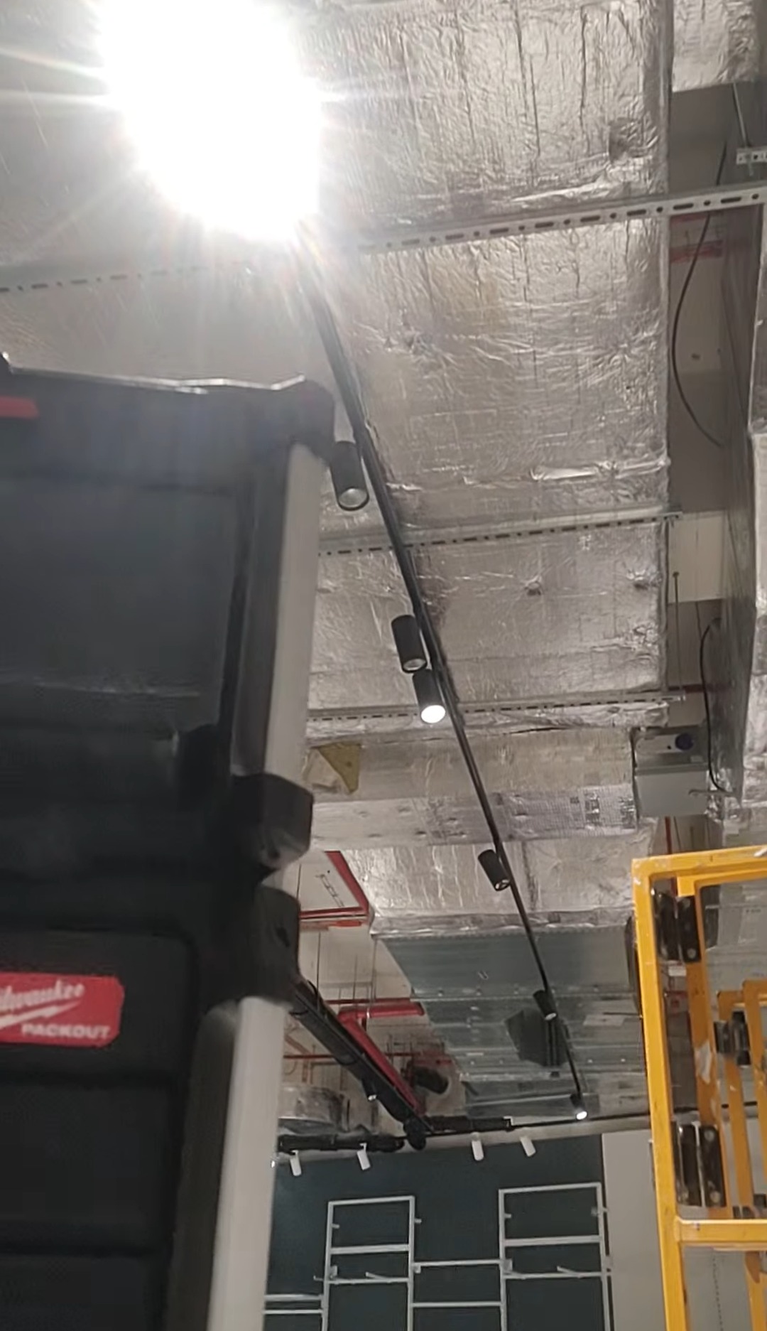 Widok na sufit z zamontowanymi reflektorami szynowymi. Widoczna instalacja, narzędzia i drabina. Ujęcie z dołu, na pierwszym planie skrzynka narzędziowa.