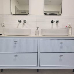 Przemysław Proczek - Nowoczesna łazienka z podwójną umywalką nablatową, bateria ścienna, lustra w czarnych ramach i szafka w odcieniach błękitu z ryflowanymi frontami szuflad.