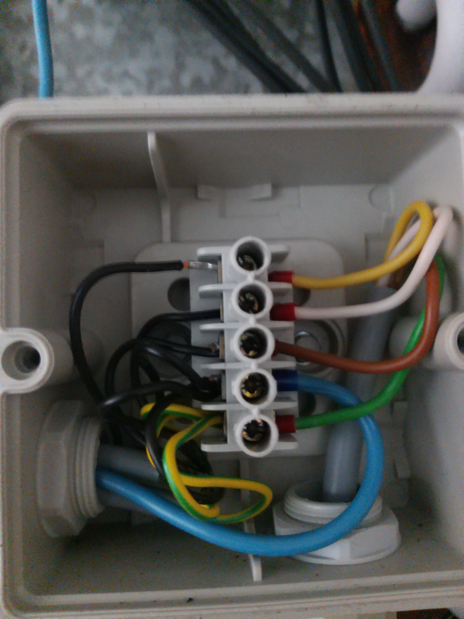 Wnętrze puszki elektrycznej z podłączonymi przewodami o różnych kolorach do listwy zaciskowej, widoczne śruby mocujące przewody.