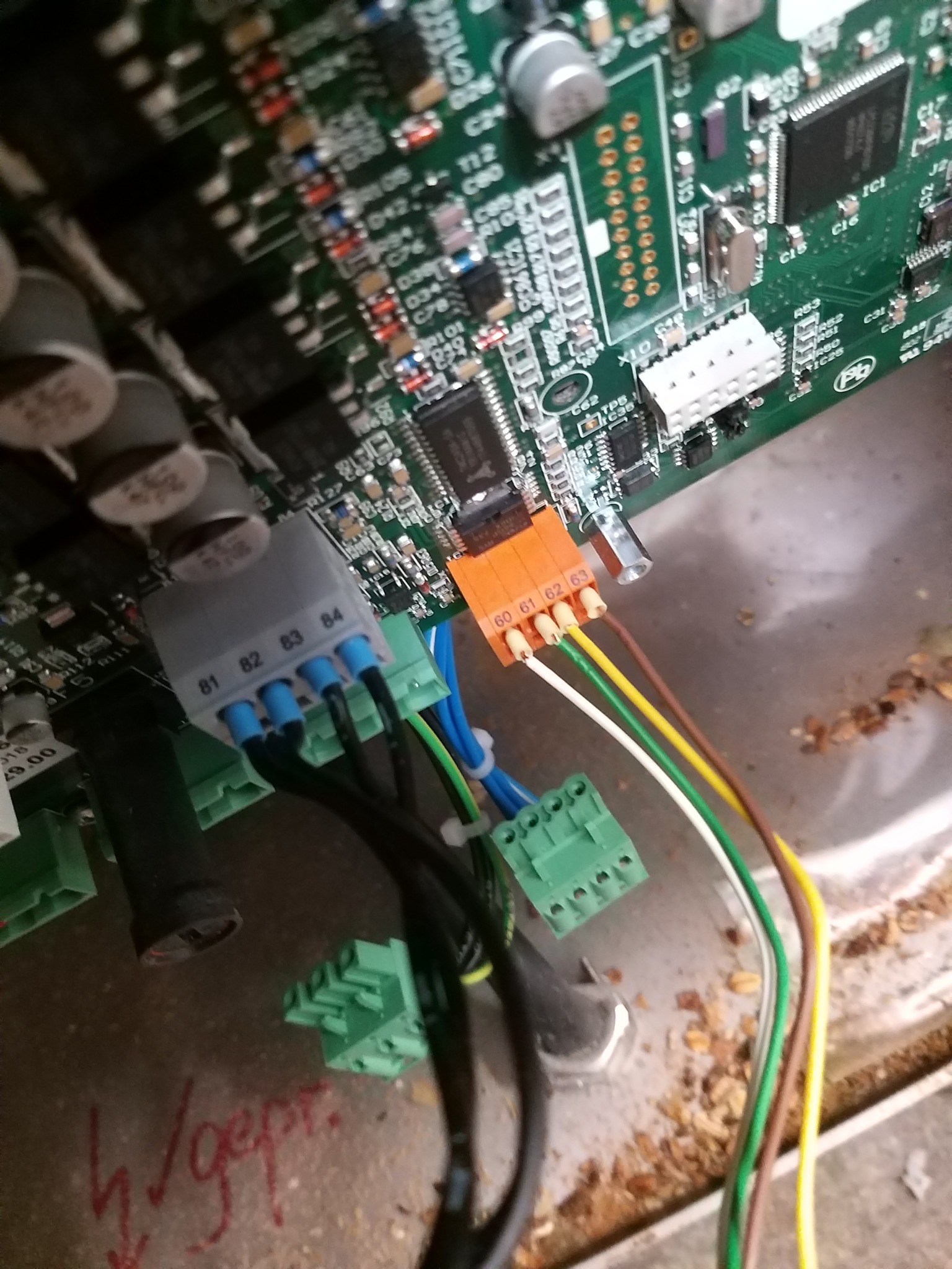 Fragment zielonej płyty głównej z widocznymi elementami elektronicznymi, złączami kablowymi oznaczonymi numerami 60-63 i 81-84 oraz przewodami w kolorach białym, żółtym, brązowym, zielonym...