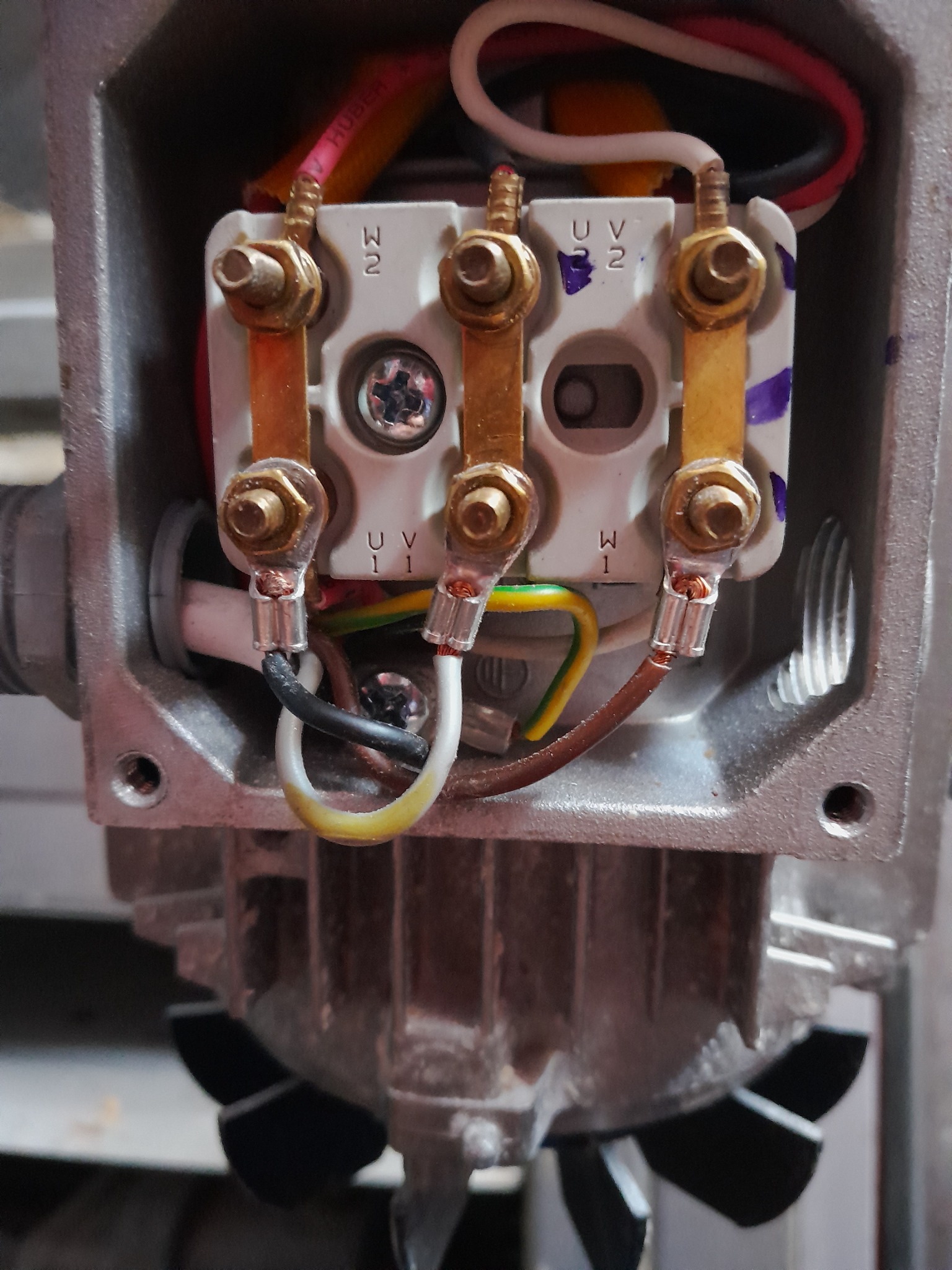 Szczegółowe ujęcie podłączenia przewodów elektrycznych do zacisków silnika elektrycznego w szarej metalowej obudowie, widoczne oznaczenia U, V, W na białej listwie zaciskowej.