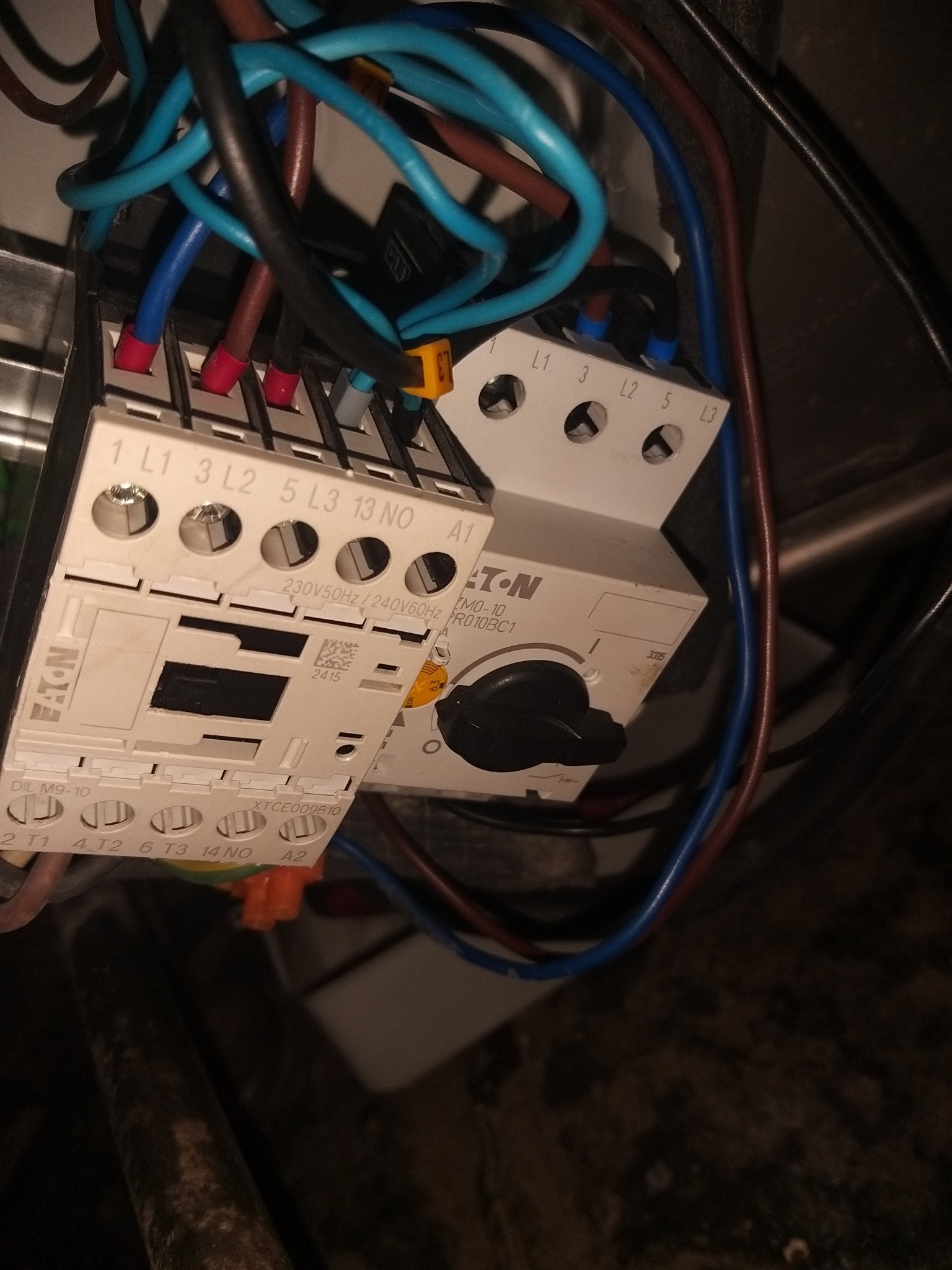 Fragment instalacji elektrycznej z przekaźnikiem Eaton DIL M9-10 i wyłącznikiem silnikowym, widoczne podłączenia kabli w kolorach niebieskim, brązowym i czarnym, z oznaczeniami L1, L2, L3, T1, T2, T3.