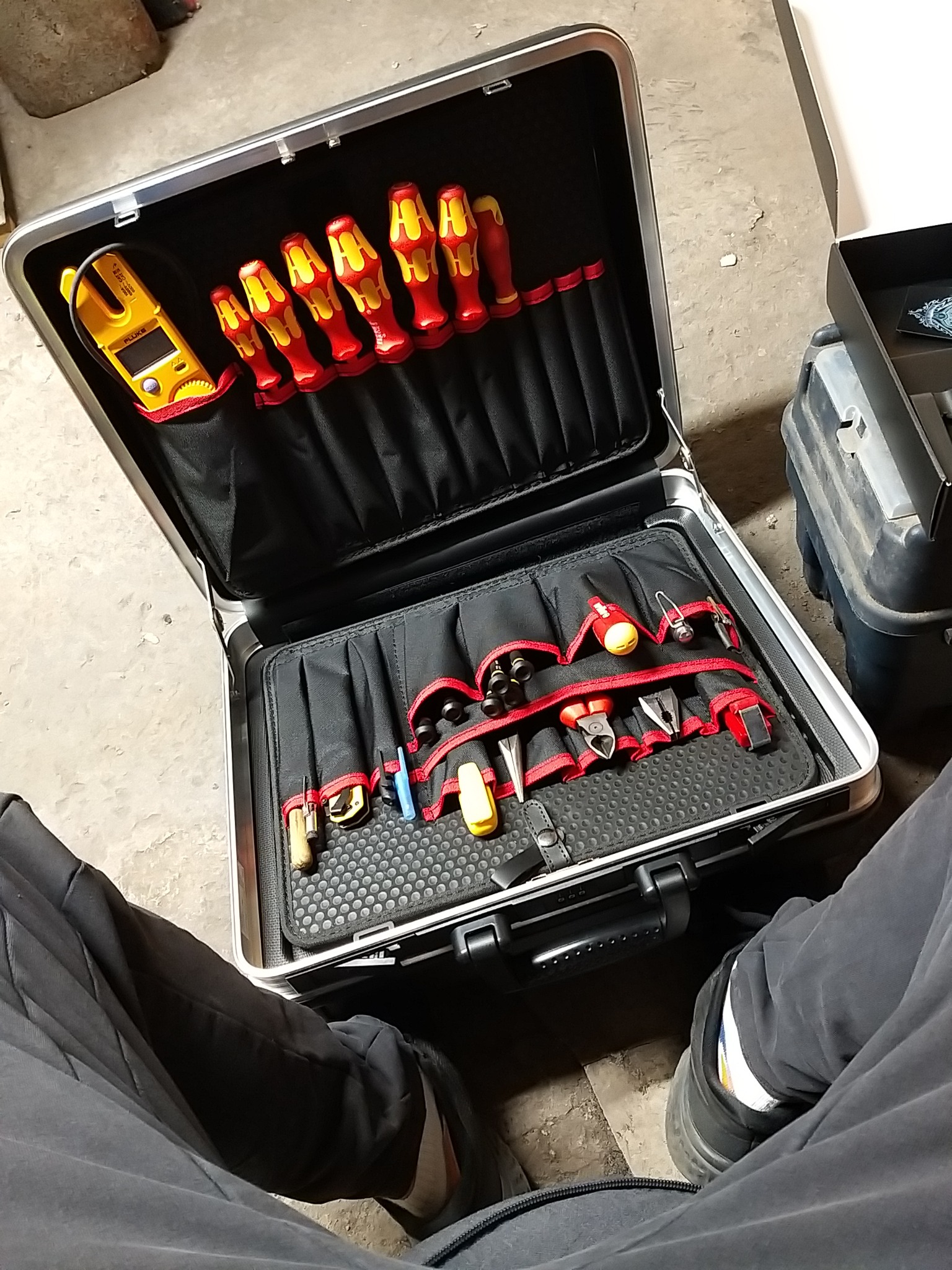 Otwarta aluminiowa walizka z narzędziami elektrycznymi, w tym izolowane śrubokręty Wera z czerwonymi i żółtymi uchwytami, miernik Fluke i różnorodne szczypce, ułożone w czarnych przegródkach...