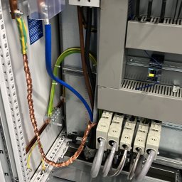 Goldfinger - Wnętrze szafy elektrycznej z widocznymi elementami instalacji: przewody w oplocie miedzianym, kable w kolorowych izolacjach, styczniki Siemens i wyłącznik.