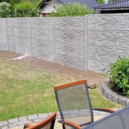 Szary, imitujący kamień, prefabrykowany system ogradzający posesję w Wałczu, widziany zza stolika ogrodowego z butelką wody mineralnej.