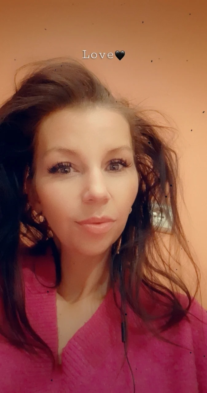 Portret kobiety z rozpuszczonymi, ciemnymi włosami, w różowym swetrze, z delikatnym makijażem i kolczykami, z filtrem 'Love'.