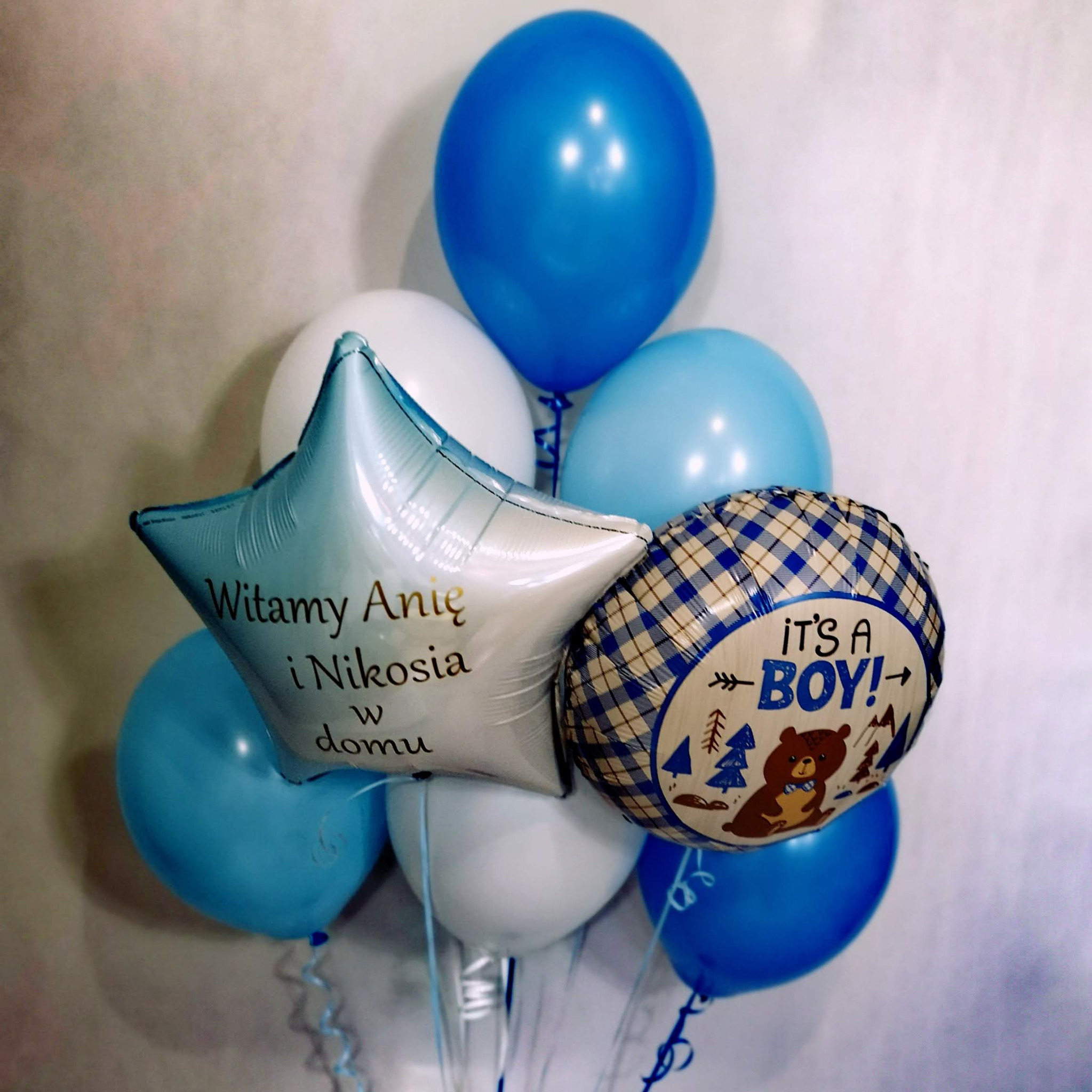 Kompozycja balonowa w odcieniach błękitu i bieli z napisem 'Witamy Anię i Nikosia w domu' na balonie w kształcie gwiazdy oraz balonem z napisem 'It's a Boy!' i rysunkiem misia.