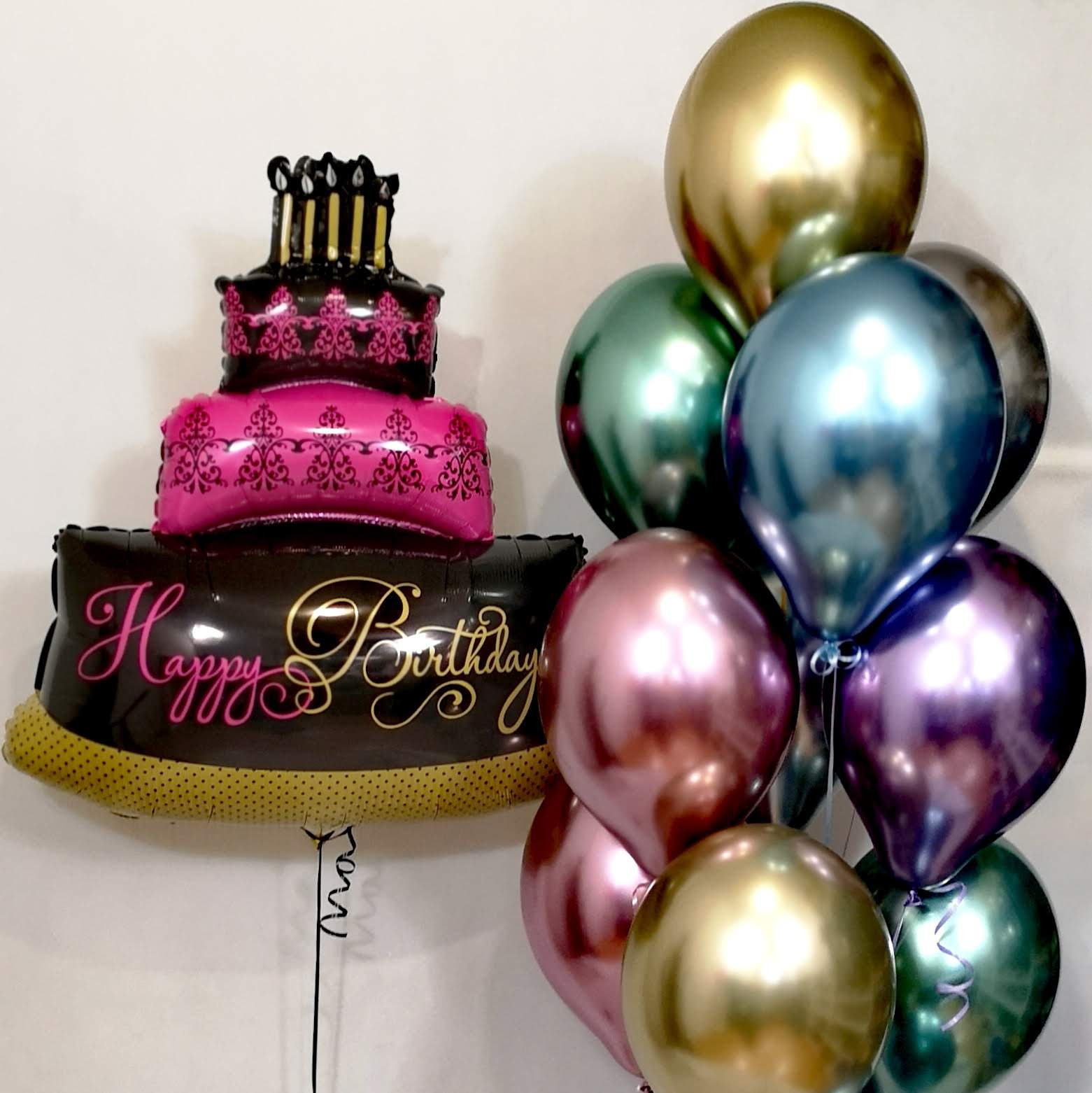 Zestaw balonów urodzinowych: balon w kształcie tortu z napisem 'Happy Birthday' oraz bukiet metalicznych balonów w odcieniach złota, zieleni, błękitu i fioletu.