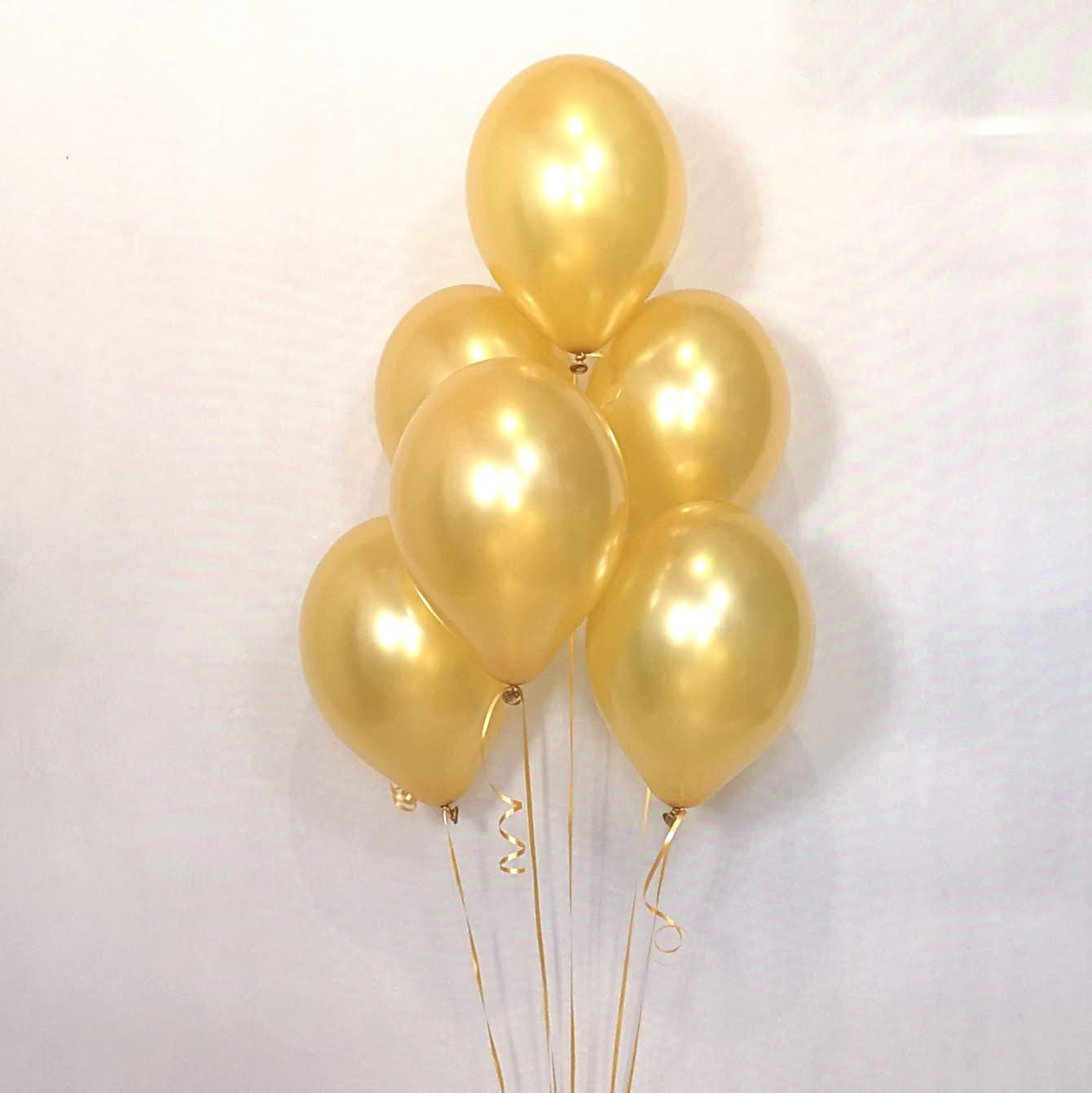 Bukiet siedmiu błyszczących, złotych balonów z kręconymi wstążkami na tle białej ściany.