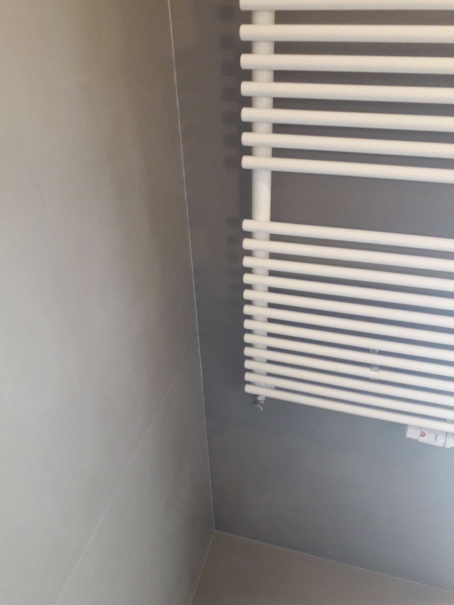 Biały, drabinkowy grzejnik łazienkowy na szarej, kafelkowanej ścianie, widok z dołu.