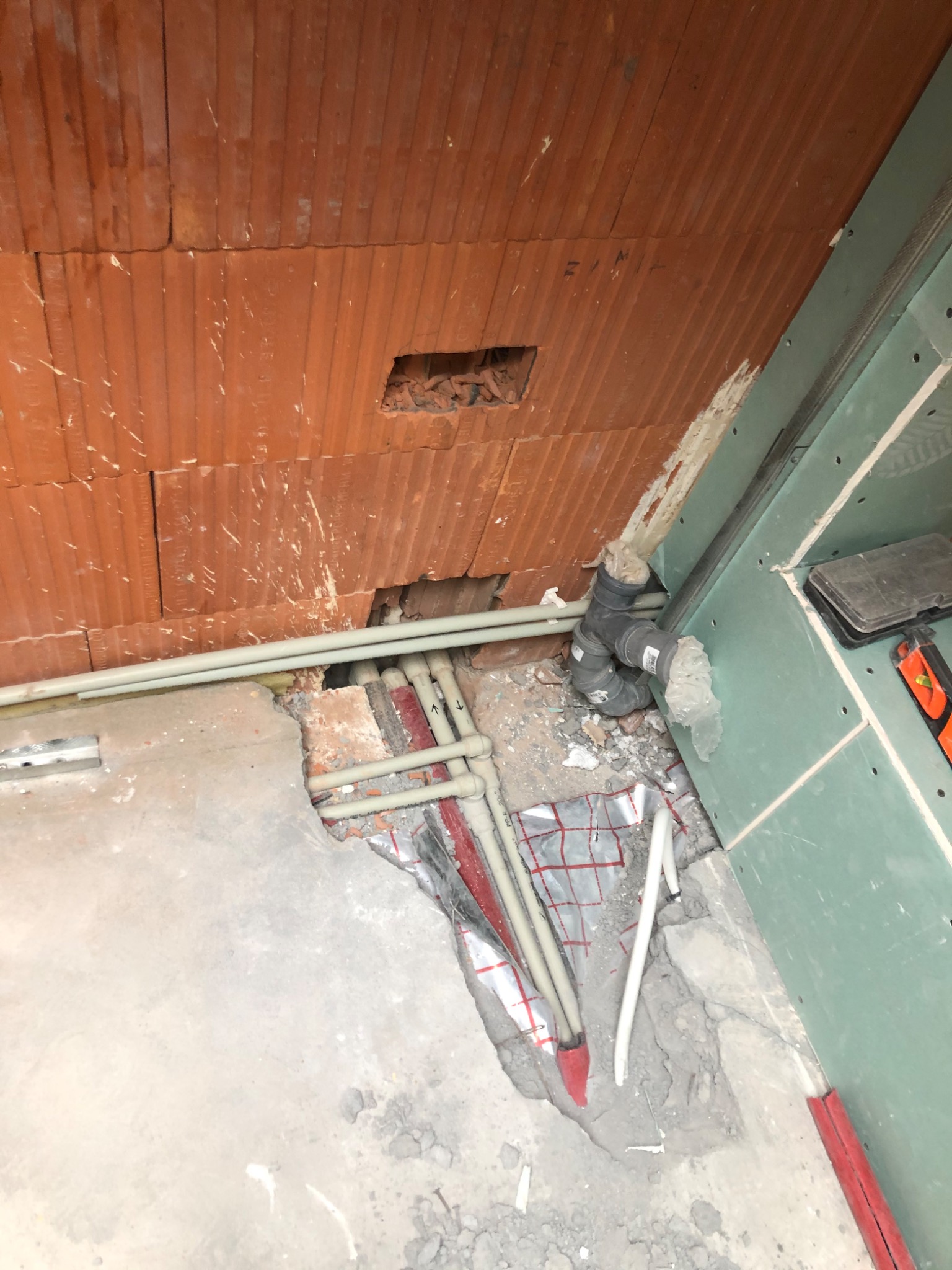 Instalacja rur wodnych i kanalizacyjnych w trakcie prac, widoczne fragmenty ściany z cegły dziurawki, płyty kartonowo-gipsowej i podłogi w stanie surowym.
