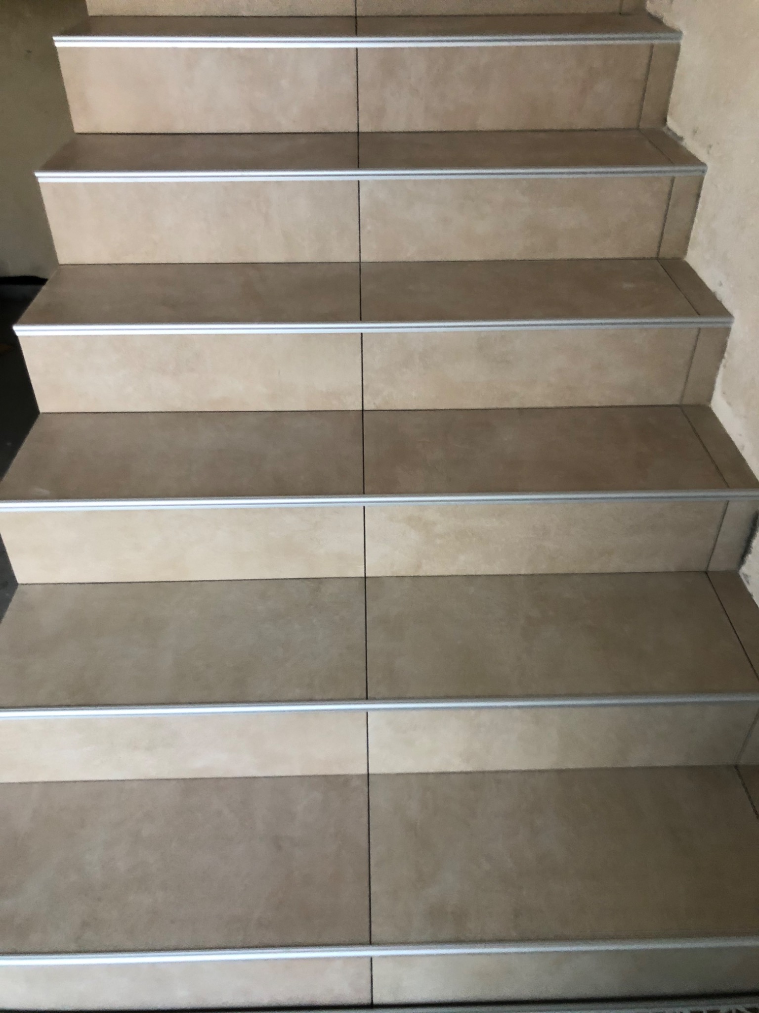 Wyłożone beżowymi płytkami schody z aluminiowymi listwami zabezpieczającymi krawędzie.