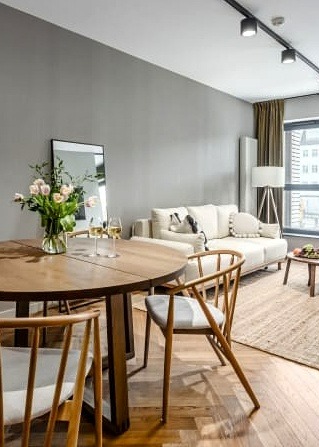 Jasne wnętrze mieszkania z drewnianym stołem, krzesłami, sofą i bukietem kwiatów w wazonie na stole, oświetlone światłem dziennym.