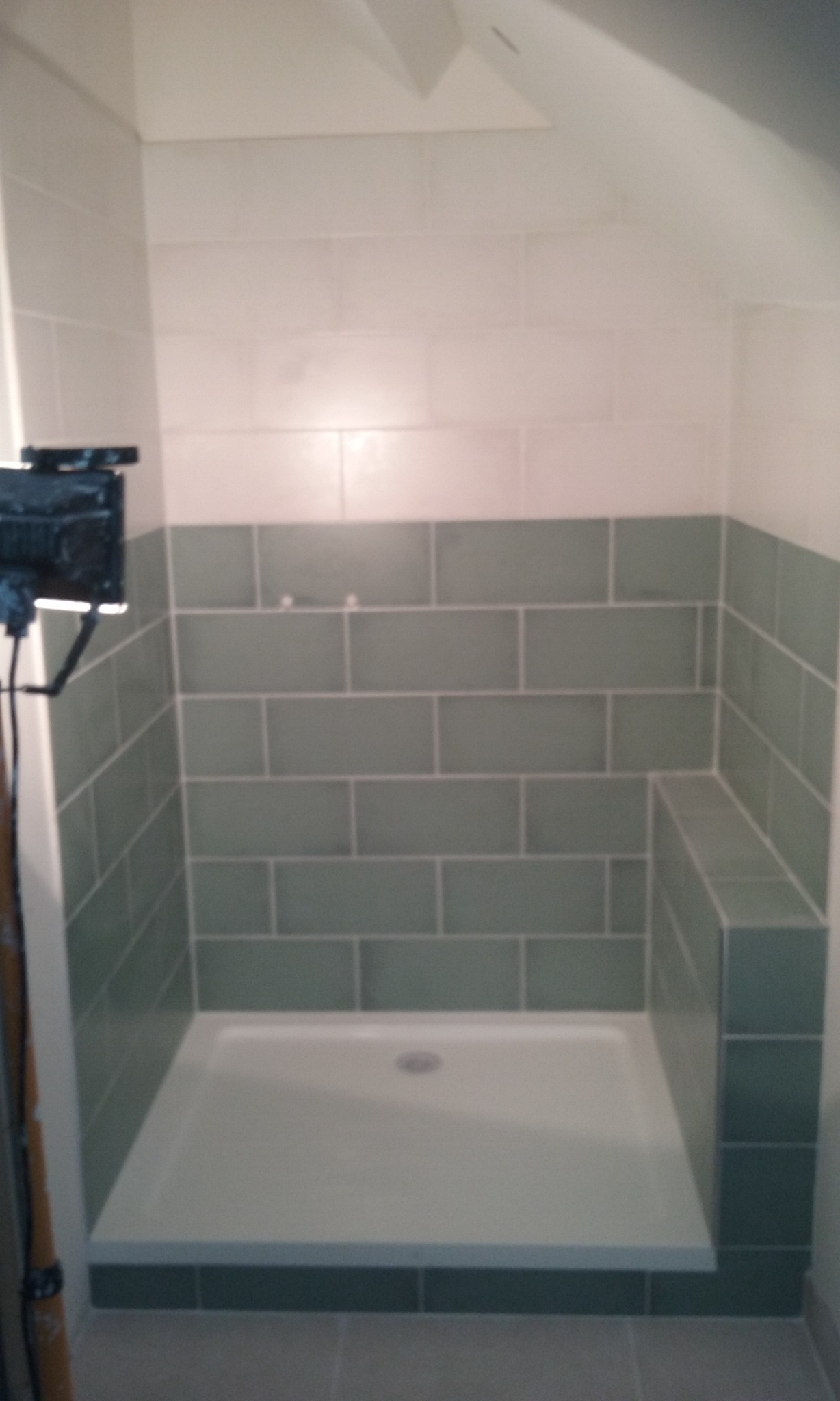 Wykończony brodzik z obłożonymi zielonymi płytkami ścianami do połowy wysokości w łazience na poddaszu.