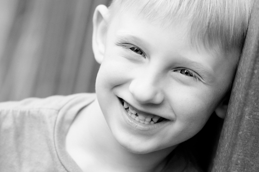 Portret uśmiechniętego chłopca opierającego głowę o ścianę, czarno-białe zdjęcie z bliska.