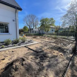 Przygotowanie terenu pod trawnik: wyrównana ziemia, obrzeża wytyczone, system nawadniania w trakcie instalacji, widok z perspektywy ogrodu.