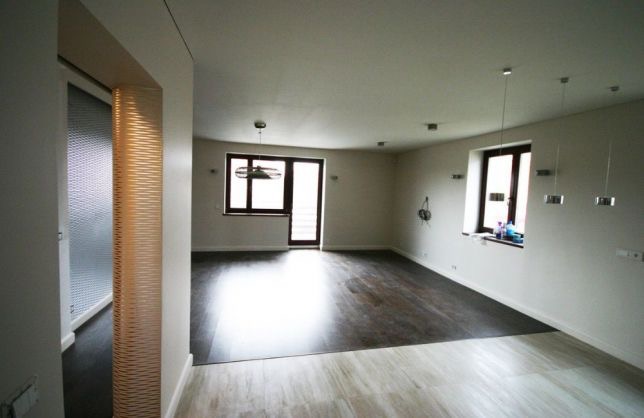 Przestronne, jasne wnętrze po remoncie z dwiema różnymi fakturami podłogi, dekoracyjną ścianką ażurową przy wejściu i nowoczesnym oświetleniem.